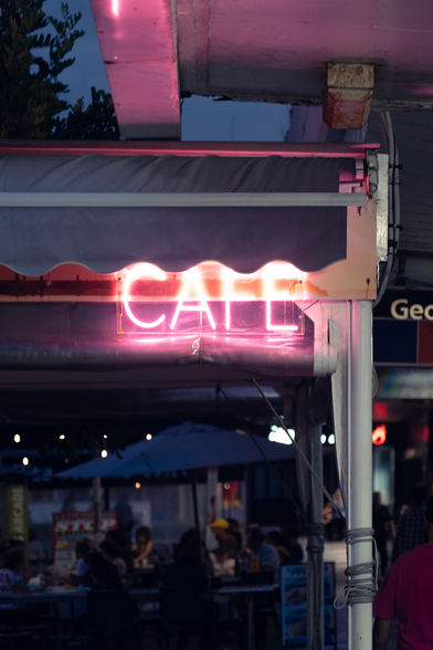 An illuminated sign of a simple lettering saying "CAFE" at an outside seating area on a sidewalk of Redcliffe (Queensland, Australia). The photo was taken in the evening