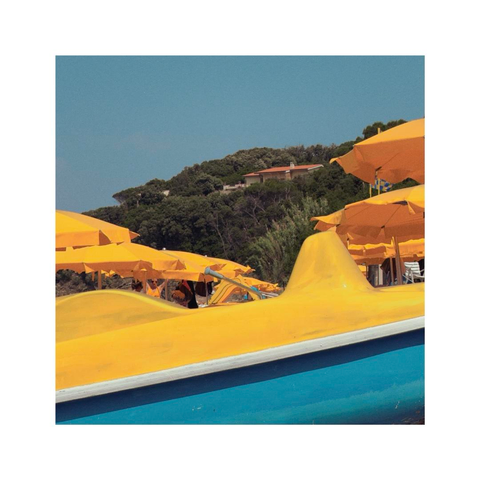 looking at all the accessories of a beach all in bright yellow colors. there are sun umbrellas and and paddleboats all stacked behind each other. in the background there's the hilly coastline with some green shrubs and trees