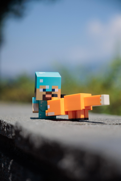 A Minecraft figurine holds an orange blocky fox, with a blurred natural background and clear blue skies.