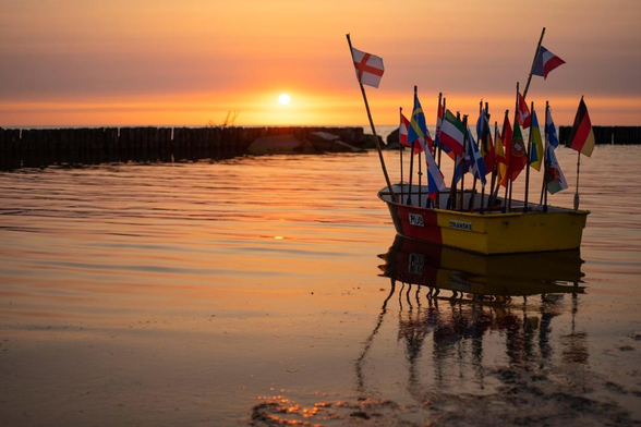 Kleines Ruderboot im Sonnenuntergang. In dem Boot stecken sehr viele verschiedene Landesfahnen. 