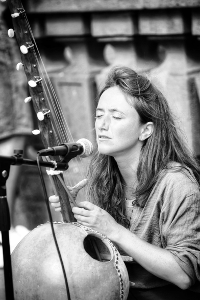 Eine junge Frau spielt eine Kamale Ngoni und singt mit geschlossenen Augen zu ihrem Spiel.