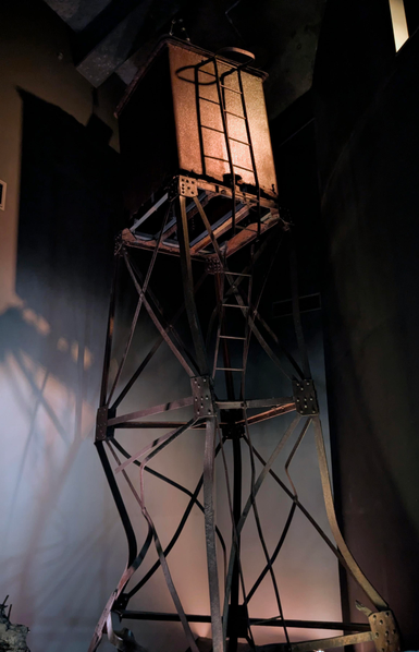 Ein eckiger Kasten auf einem Turm mit verbogenen Streben. 
Gelblich-blaues Licht.