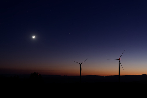 A dusk landscape features a crescent moon in a darkening sky with two silhouetted wind turbines.