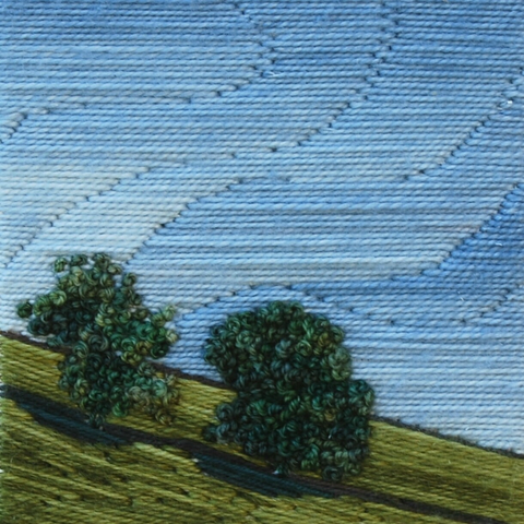 Stitched artwork depicting hillside with two trees, blue sky