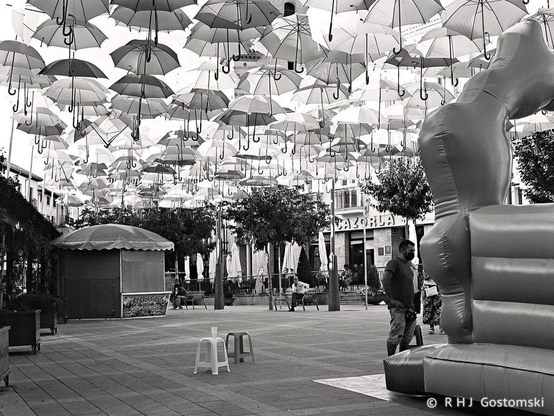A black and white photo of a plaza in Cazorla during Fiesta week, with a sea of umbrellas hanging above