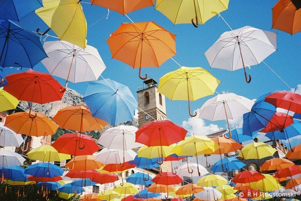 A colour film photo of a sea of brightly coloured umbrellas above Plaza de la Corredera in Cazorla. A church bell tower peeks through between the umbrellas.