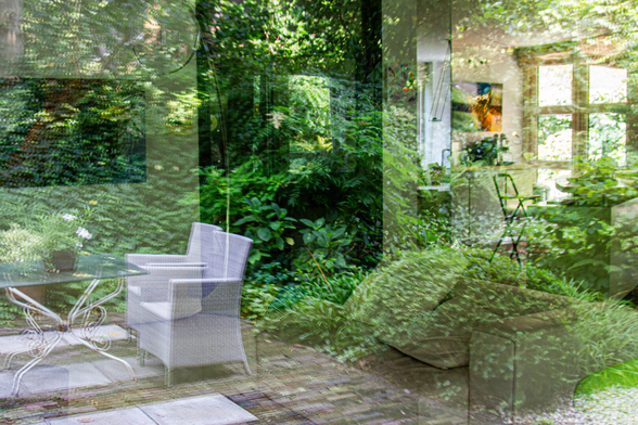 My garden is reflected in the living room window. Below left, a stone patio with two chairs and a garden table; above that, the outline of a painting peeks through the faint foliage. Below right, a leather sofa covered with the leaves of a boxwood ball. Above that, in the distance on the right, the kitchen, with a painting on the wall, doors to the garden, a bar stool, a bar, and a lamp hanging from the ceiling. In the top center, the door to the hallway, where the garden is reflected again.