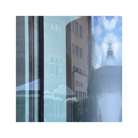 detailed look at a facade made entirely out of glass reflecting the houses nearby and the blue sky with some bright clouds