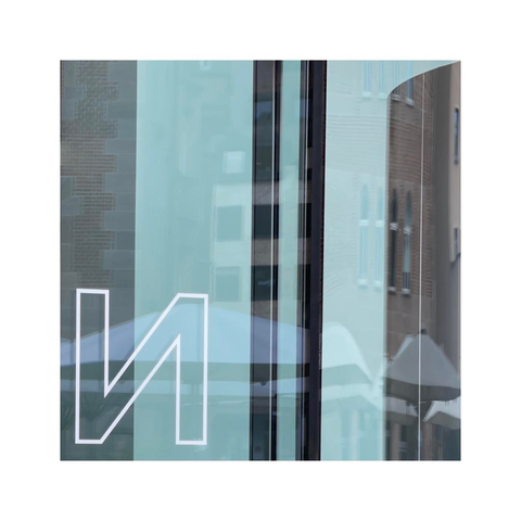 a detailed look at a facade made entirely out of glass reflecting the houses nearby and the blue sky with some bright clouds. there's a white sticker on the glass with a capital letter n in the bottom left corner of the frame