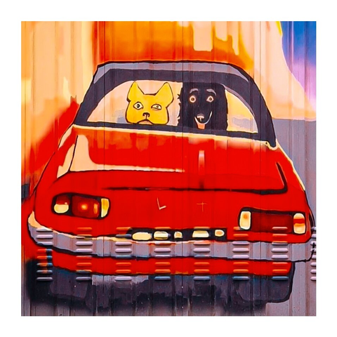 A close up of the red vintage car - focusing on the dogs looking out the rear window. The yellow dog is  has an almost exasperated expression, while the black dog looks like it doesn't have any brain cells. The background features an abstract blend of orange and blue colours.