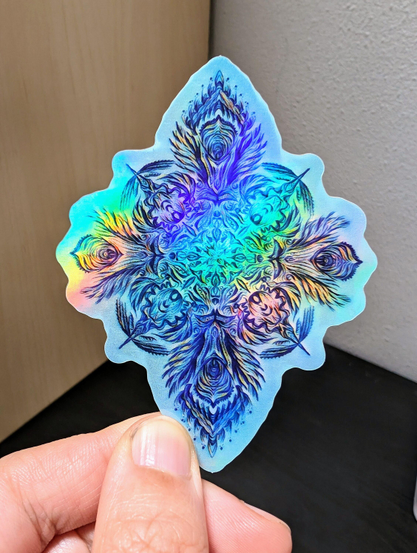 Photo of a left hand holding a diecut sticker. The sticker is a holographic mandala drawing.