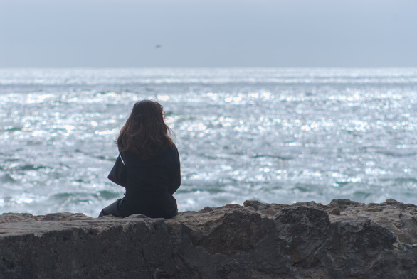 A silhouette of a woman sitting on a wall, looking at the ocean
