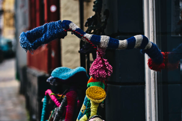 Ein Fahrrad steht an eine Hauswand angelehnt. Das Fahrrad ist von oben bis unten in bunte Wolle eingestrickt. Lenker, Bremshebel, Sattel, Rahmen, Lampe, einfach alles! Man nennt es wohl Guerilla knitting... 