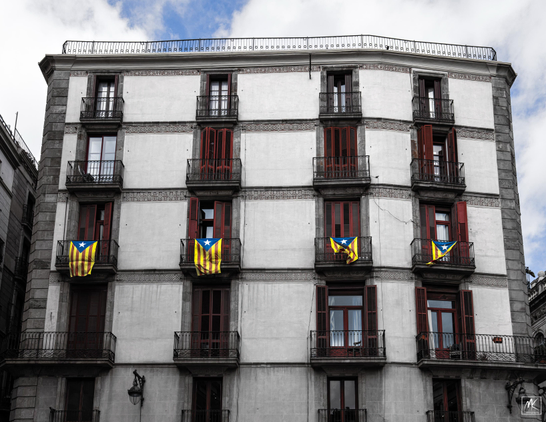 Color photo of a building facade with a row of Catalan L'Estelada flags hanging down from the balconies of the second floor.
