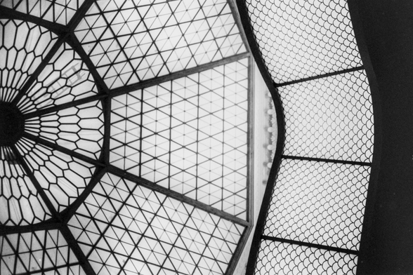 Black&White photo of geometric shapes, the left ⅔ is shades of light with black beams splitting it into hexagon at the left edge and triangles in each slice. The right ⅓ is a wavy bright panel with overlaid overlapping circular mesh which makes it look like fish scales.