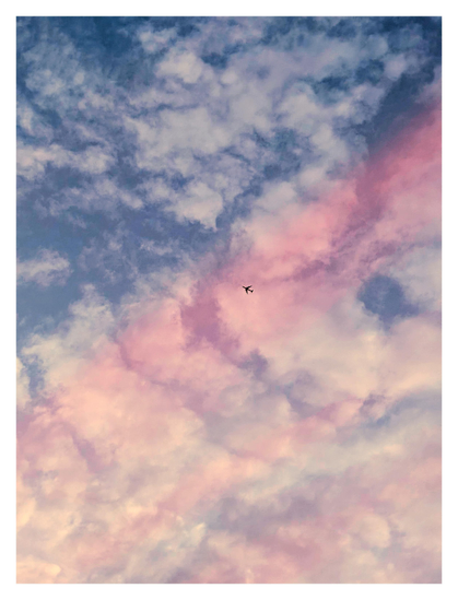 Wide, arcing bands of red light stretch across a blue evening sky with clouds. Inside the widest band is the tiny, distant silhouette of an airplane.