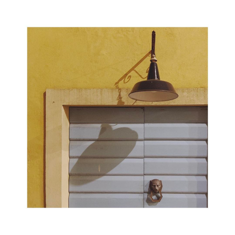 an old circular metal street lamp is hanging over a closed wooden door. the structure of the lamp is casting some interesting shapes of shadows on the door. the door is colored in light blue while the wall is painted in yellow