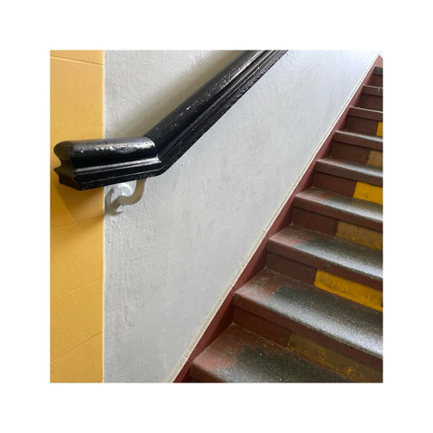 detail of some old stairs. the angled view is showing parts of the wooden handrail on the wall and parts of the steps. a part of the wall is painted in bright yellow