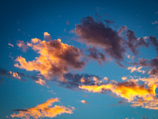 The image depicts a sky during sunset, with a deep blue background. The clouds are scattered across the sky, with some appearing darker and more ominous, while others are illuminated by the warm, golden light of the setting sun. The clouds closest to the sun are bathed in a vibrant orange and yellow glow, creating a striking contrast against the blue sky. The clouds vary in shape and size, with some appearing fluffy and others more wispy. The overall effect is a beautiful and dynamic scene, showcasing the natural beauty of the sky at dusk.

Provided by @altbot, generated privately and locally using Ovis2-8B