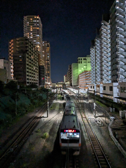 Ein Local Train (Nahverkehrszug) verlässt bei  Dunkelheit den Bahnhof von Kokubunji.

Links und rechts stehen Hochhäuser.

Das Bild wurde von einer Brücke aufgenommen.
Der Zug schickt sich gerade an darunter her zu fahren. 