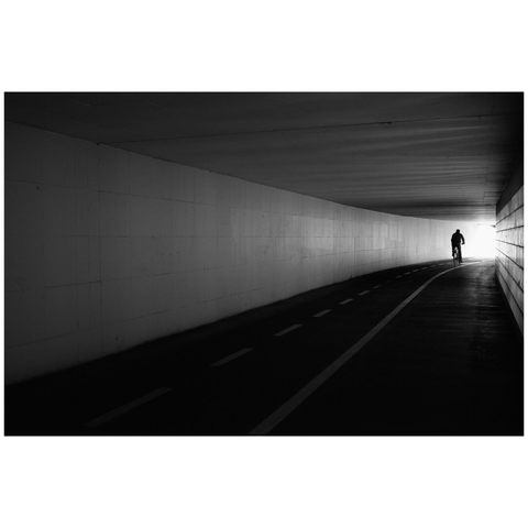 A subway for cycilst and pedestrians. Only a single cyclist is in the frame at the end of the subway, contrasted against the outside light.