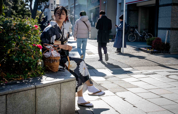 Noia amb quimono asseguda en un passeig de Kamakura, mira a la càmera.