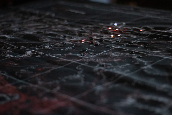 The same map is displayed. More white topographic outlines are visible, along with some red lines and shapes representing roads and other infrastructure. Some LEDs are also lit.