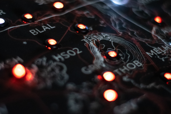 Close up of the map and LEDs. You can see the texture of the fabric and the details of the design. Each LED (attached to the map) has a printed text under or above it. The texts we can see on the photo: BLAL, HS02, THNA, THOB, MELH. These are names of GPS stations that are used to measure earthquakes in Iceland.