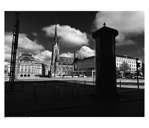Schwarzweißfotografie: Innenstadt, Aufnahme von links nach rechts: Opernhaus, Petrikirche (neogotischer Kirchenbau mit Turm, Chemnitzer Hof (Hotel) davor lange dunkle Schatten auf dem Fußweg und eine Litfaßsäule 