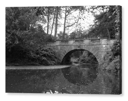Black and white photograph showing a small stone bridge over calm water.  The image is shown printed upon a block canvas.