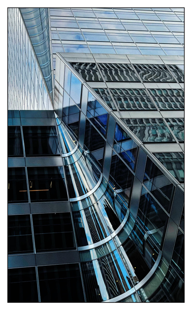 Closeup of the facade of the Bank of China office tower at 7 Bryant Park in Manhattan, a glass-and-steel skyscraper of many reflective windows, viewed from an askew angle at street level. The upper portion of the building is set back from the lower one. Strikingly, two conical incisions are carved into a corner of the tower: the lower cone pointing up, the upper one pointing down, narrowing to where their apexes meet at the setback level to create an hourglass effect. From the angle of the photo it also appears as a kind of starburst, with the building’s lines all converging on a vanishing point. The windows of the lower part of the tower reflect distorted images of other windows and buildings, while the upper part reflects white clouds in a blue sky.
h/t Architect Magazine for help with the description:
https://www.architectmagazine.com/project-gallery/bank-of-china-at-7-bryant-park/