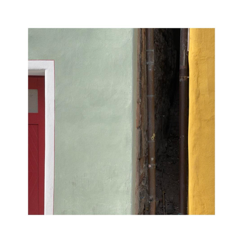 looking at the narrow gap in between two old town houses. the house on the left is painted in lime green and has a red door, the house on the right is painted in yellow. the view is focused on the little details and has an almost abstract feel