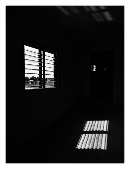 A dark room with sunlight streams through a louvered window.