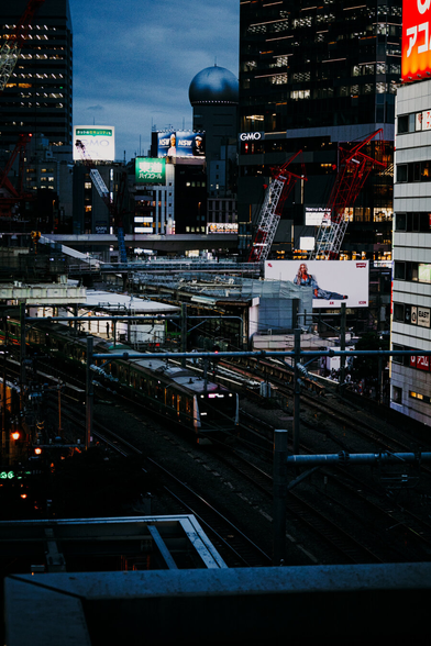 photo of the tracks of the Shibuya train station in Tokyo by night. Lots of details in this photo, from the leaving train and the city skyline in the background.