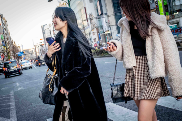 Dues dones amb cabells llargs, abillades amb abrics i portant bossa de mà travessen un carrer de Kabukicho a Tòquio.