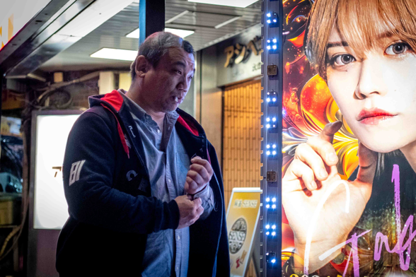Home adult amb una cigarreta a la boca, passa davant d'un anunci lluminós de bar de hostos a Kabukicho.
