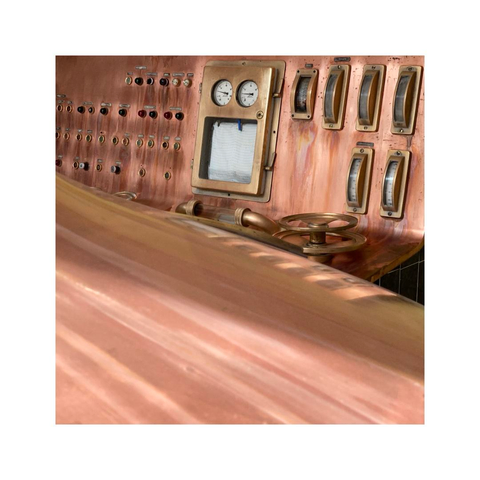 a detailed look at a control desk of a local brewery. the desk as well as the brewing copper in from of it are completely made out of shiny copper