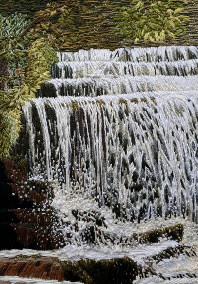 Stitched artwork depicting a waterfall and foliage on the bank