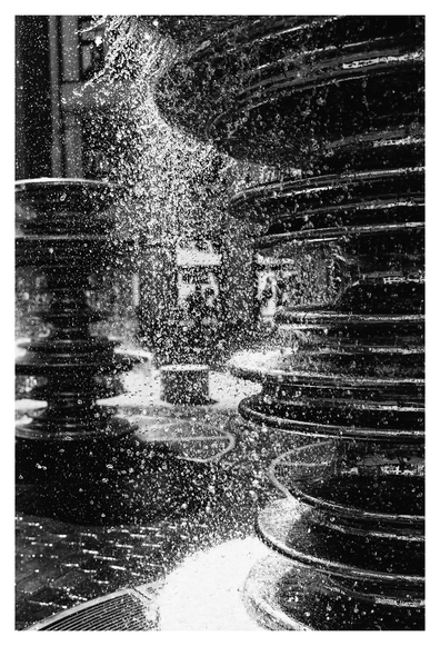 Brunnen aus spindelförmigen Strukturen, Wasser sprudelt herab, hochkontrast Schwarz/Weiß.