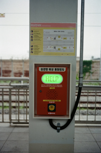 병점역 플랫폼 기둥에 '승강장 비상 통화장치'가 달려있다. 빨간색 외장에 커다란 HELP 글씨가 초록색으로 빛나고 있다.