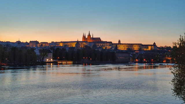 Farbfoto im Panoramaformat. Zu sehen ist ein Blick über die Moldau in Prag auf den Hradschin. Der Himmel ist noch leicht rosa vom Sonnenuntergang.