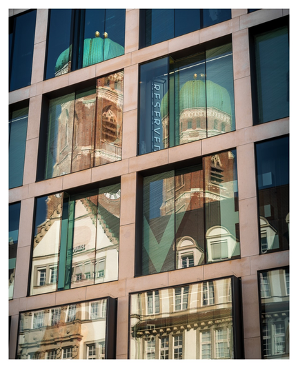 Die Doppeltürme einer Kirche spiegeln sich in den Fenstern eines großen Hauses.