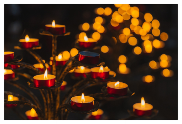 Ein Rudel friedlich leuchtender Teelichter auf einem Kerzenständer. Im Hintergrund Bokehballsgalore.