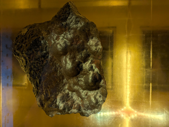 Ein Bruchstück des Gibeon-Meteoriten, der in Namibia gefunden wurde, wird durch gelbes, kreuzförmiges Licht angestrahlt. 