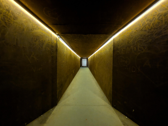 Ein Gang mit Wänden aus dunklem Metall.
An der Decke zwei Lichtstreifen, die den ganzen Gang entlang verlaufen. 