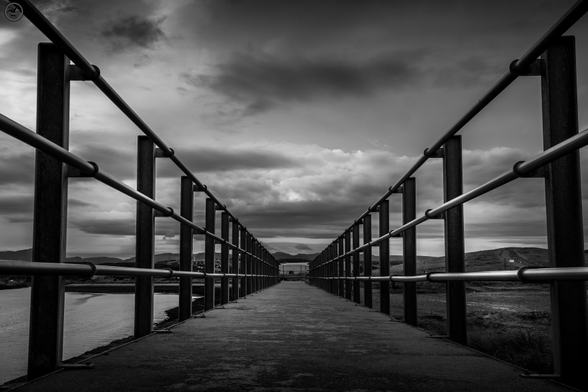 parallel railings along concrete coastal path, with cloudy skies above