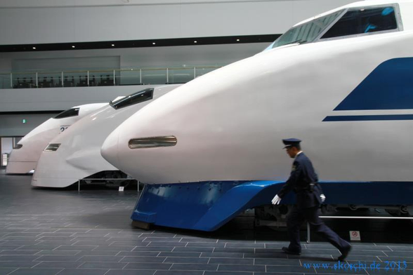 3 aufgereihte Shinkansen Triebköpfe. Davor versucht das Aufsichtspersonal aus dem Bild zu laufen. 
