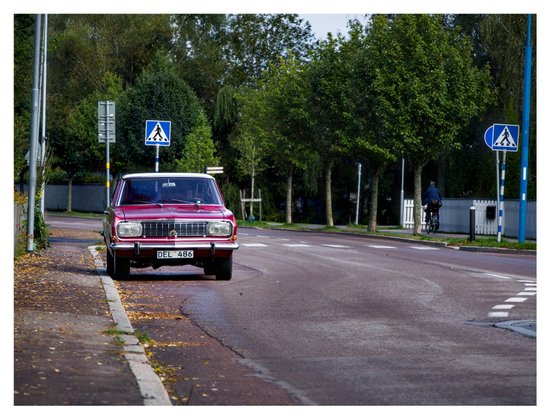 En liggande bild på en röd Opel Rekord Coupé med vitt tak. Den står parkerad vid trottoaren och ses framifrån.