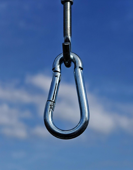 A photo of a shiny metal carabiner attached to  an equally shiny hook hanging seemingly from a  blue sky with some clouds.

