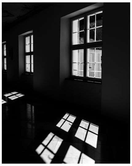 Fenster mit weißen Sprossen, viel Schatten, Lichtkleckse auf dem Boden. 